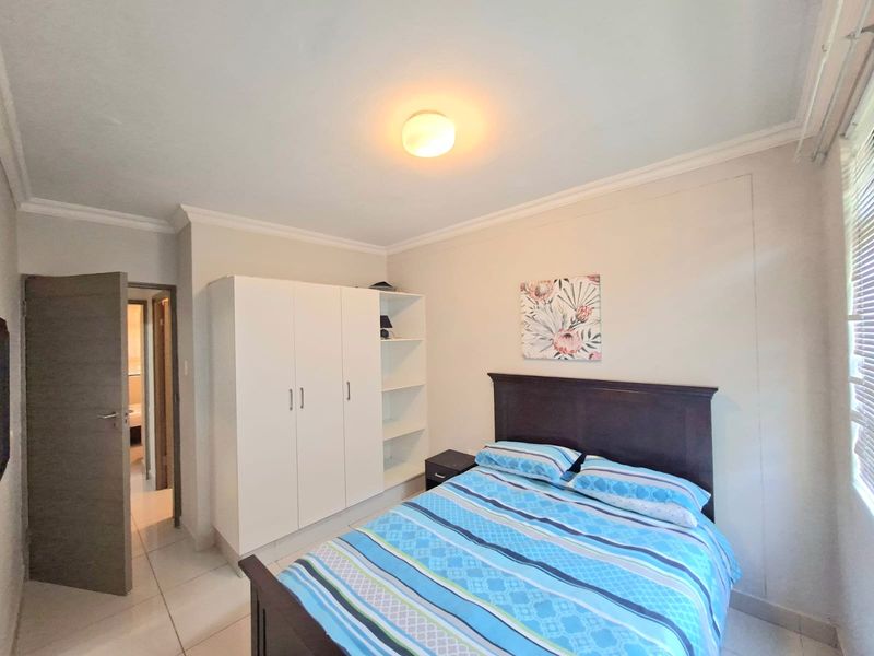 A functional bedroom featuring tiled flooring, a built-in wardrobe with open shelving, and neutral wall finishes.