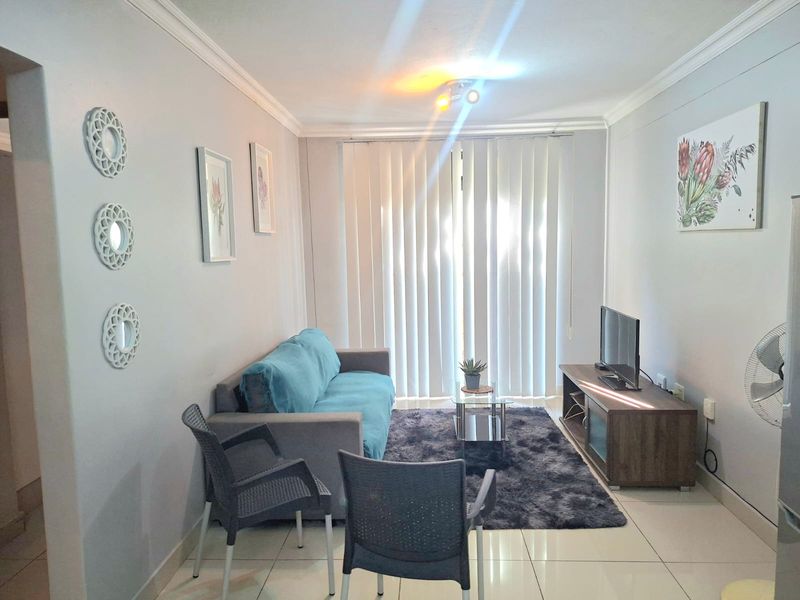 A bright living room featuring tiled flooring, cove cornicing, and vertical blinds leading to an outdoor area.