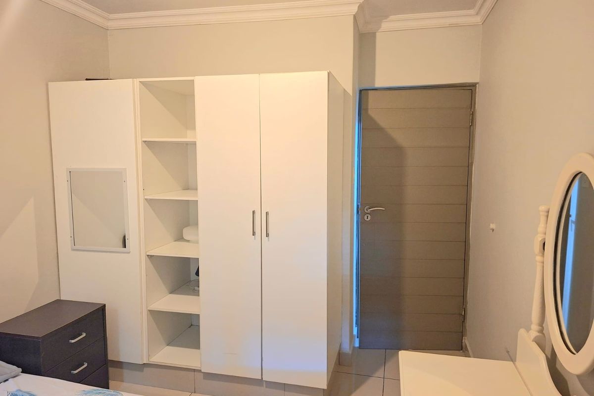 A bedroom featuring a white built-in wardrobe with open shelving, crown molding, and tiled flooring.