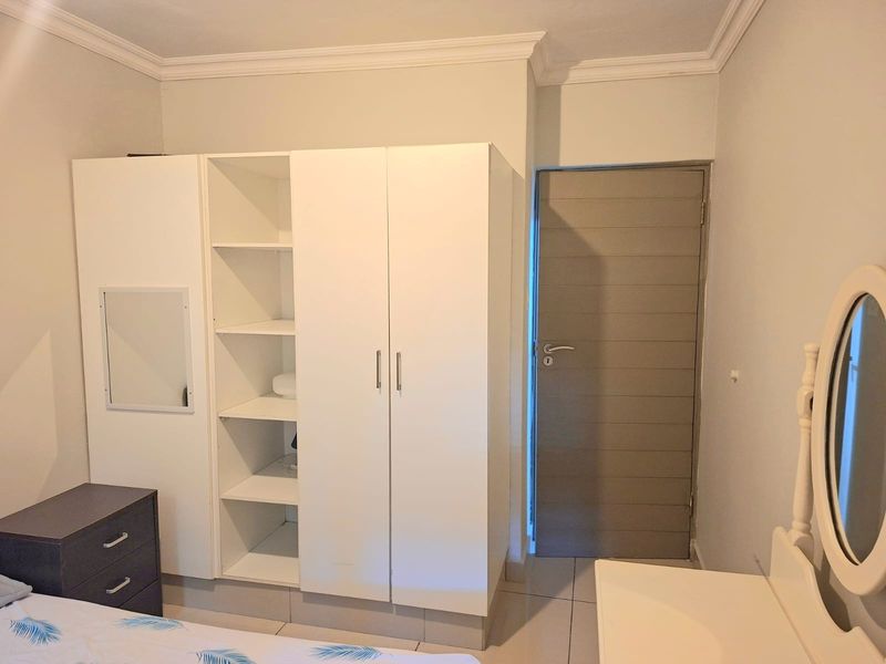 A bedroom featuring a white built-in wardrobe with open shelving, crown molding, and tiled flooring.