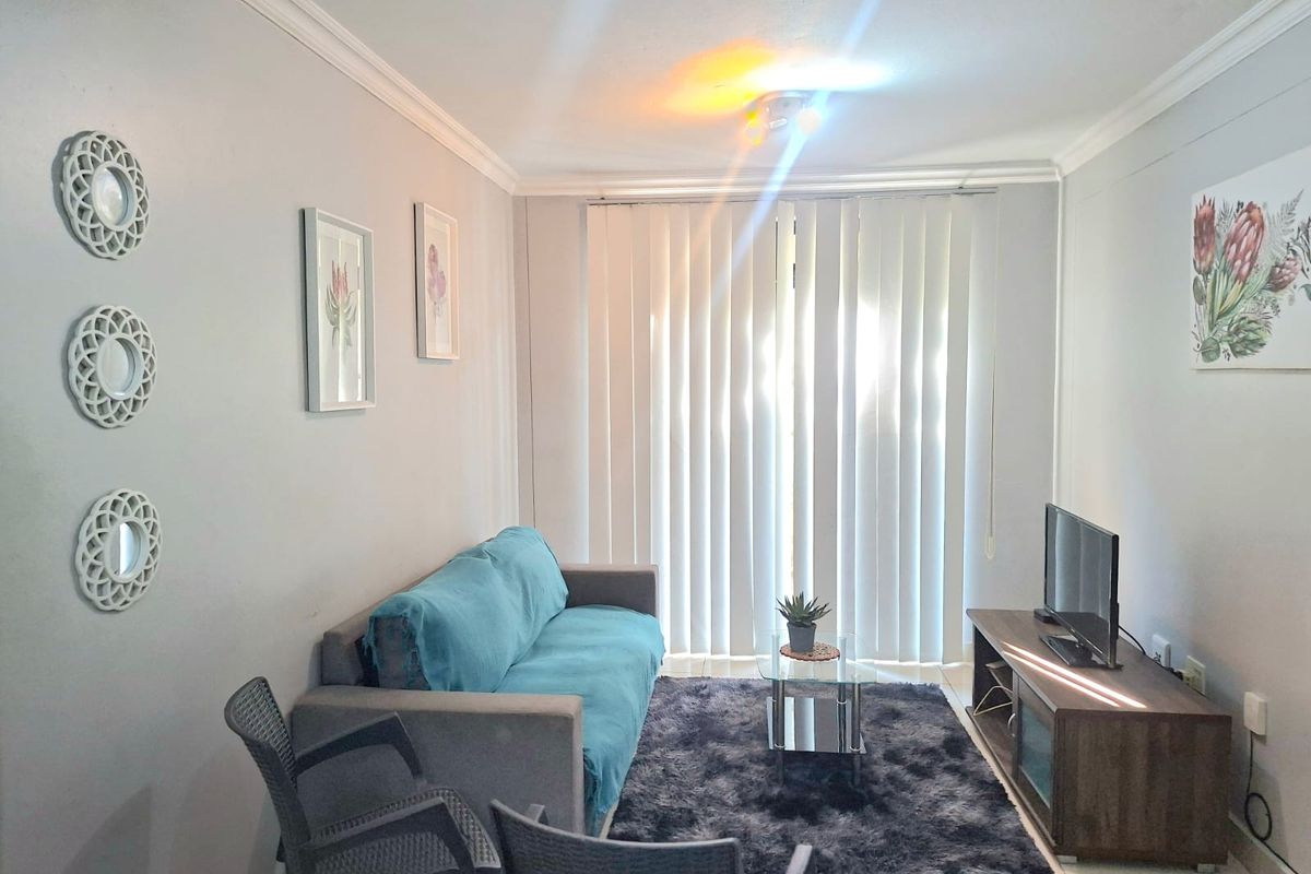 A comfortable living room featuring tiled flooring, crown molding, and vertical blinds leading to an outdoor area.