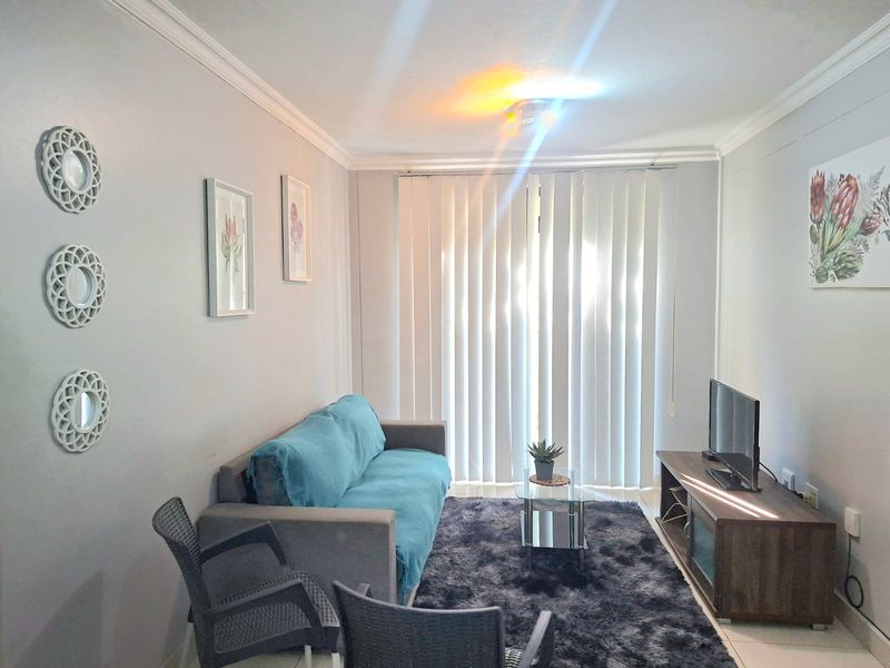 A comfortable living room featuring tiled flooring, crown molding, and vertical blinds leading to an outdoor area.