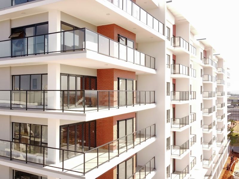 Modern apartment building exterior featuring multiple levels with glass-fronted balconies and a combination of white render and exposed brick finishes.