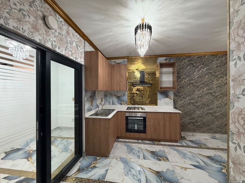Modern kitchen featuring wood-finish cabinetry, gold-tiled backsplash, built-in oven and hob, and striking marble-patterned floor tiles.