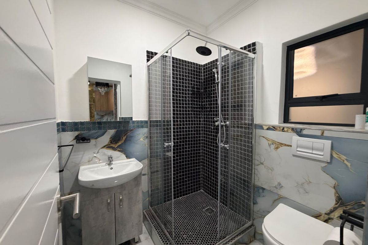 Modern bathroom featuring a glass shower enclosure with black mosaic tiling, a wall-mounted toilet, and a vanity basin with decorative marble-effect wall tiles.