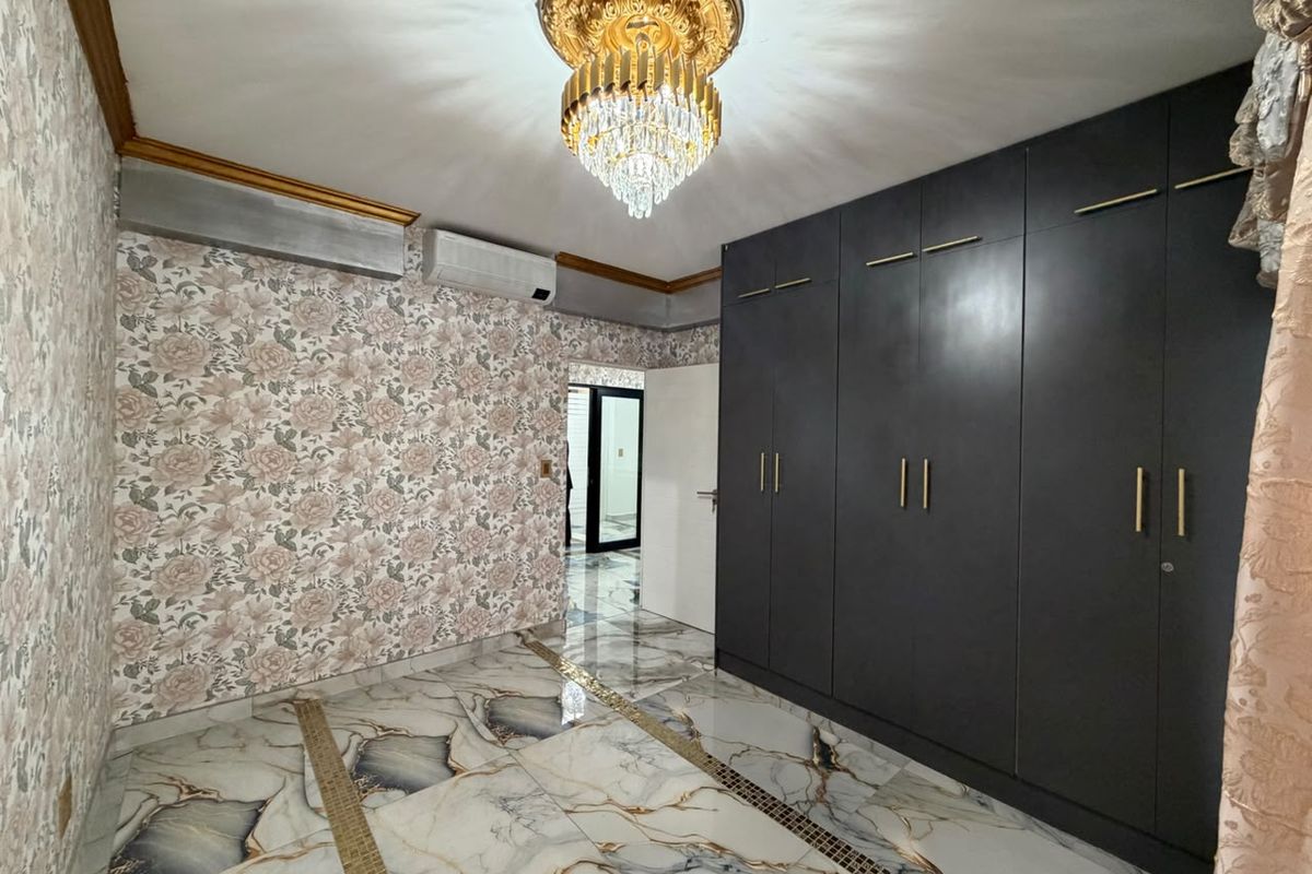A spacious bedroom featuring high-gloss marble-effect flooring, extensive built-in dark cabinetry, and a decorative chandelier, offering a clean and modern aesthetic.