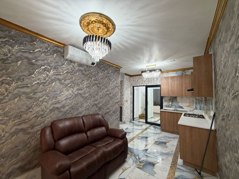 Open-plan living and kitchen area featuring marble-effect flooring, decorative ceiling fixtures, wood-tone cabinetry, and a gas hob, creating a distinctively styled interior space.