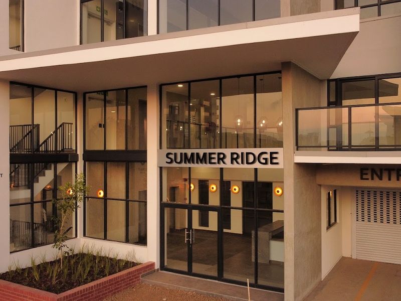 Modern apartment building entrance featuring a glass facade, concrete architectural elements, and a secure roller shutter garage access point.