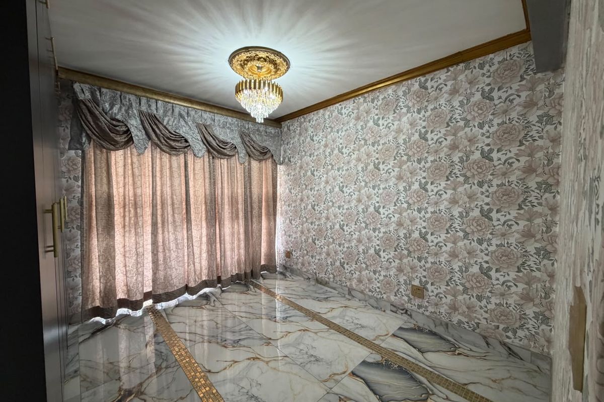 An empty living room featuring polished marble flooring with decorative inlays, floral wallpaper, gold crown molding, and a central crystal chandelier.