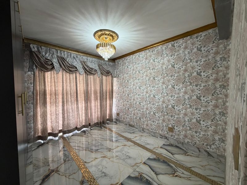 An empty living room featuring polished marble flooring with decorative inlays, floral wallpaper, gold crown molding, and a central crystal chandelier.