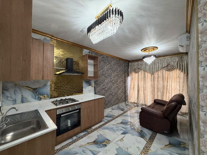 Modern open-plan kitchen and living area featuring marble-effect flooring, gold mosaic backsplash, built-in cabinetry, and elegant crystal chandelier lighting.