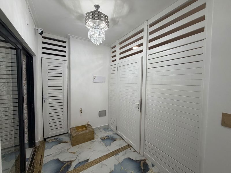 A bright, modern hallway featuring decorative tiled flooring, louvered doors, and a stylish chandelier, providing a clean and well-maintained transition space.