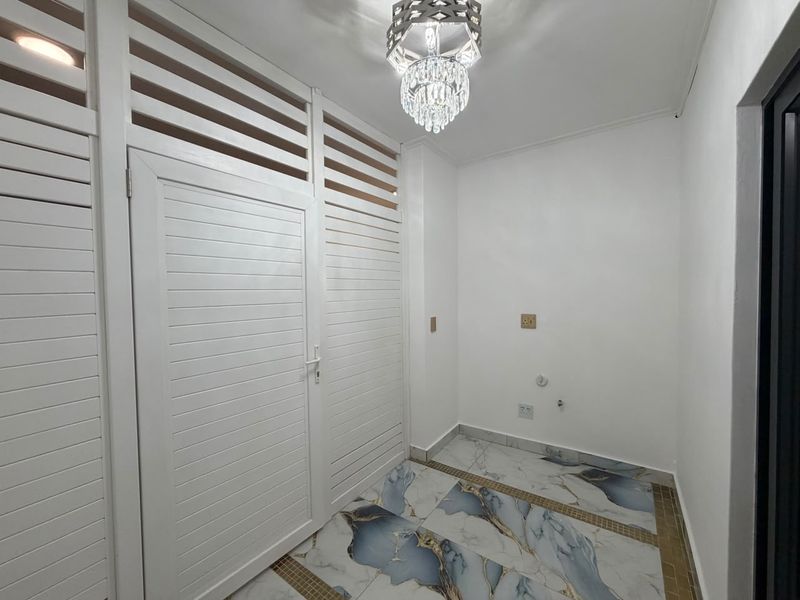 A clean, empty laundry area featuring decorative marble-effect floor tiles, louvered doors, and modern lighting, equipped with necessary plumbing and electrical connections.