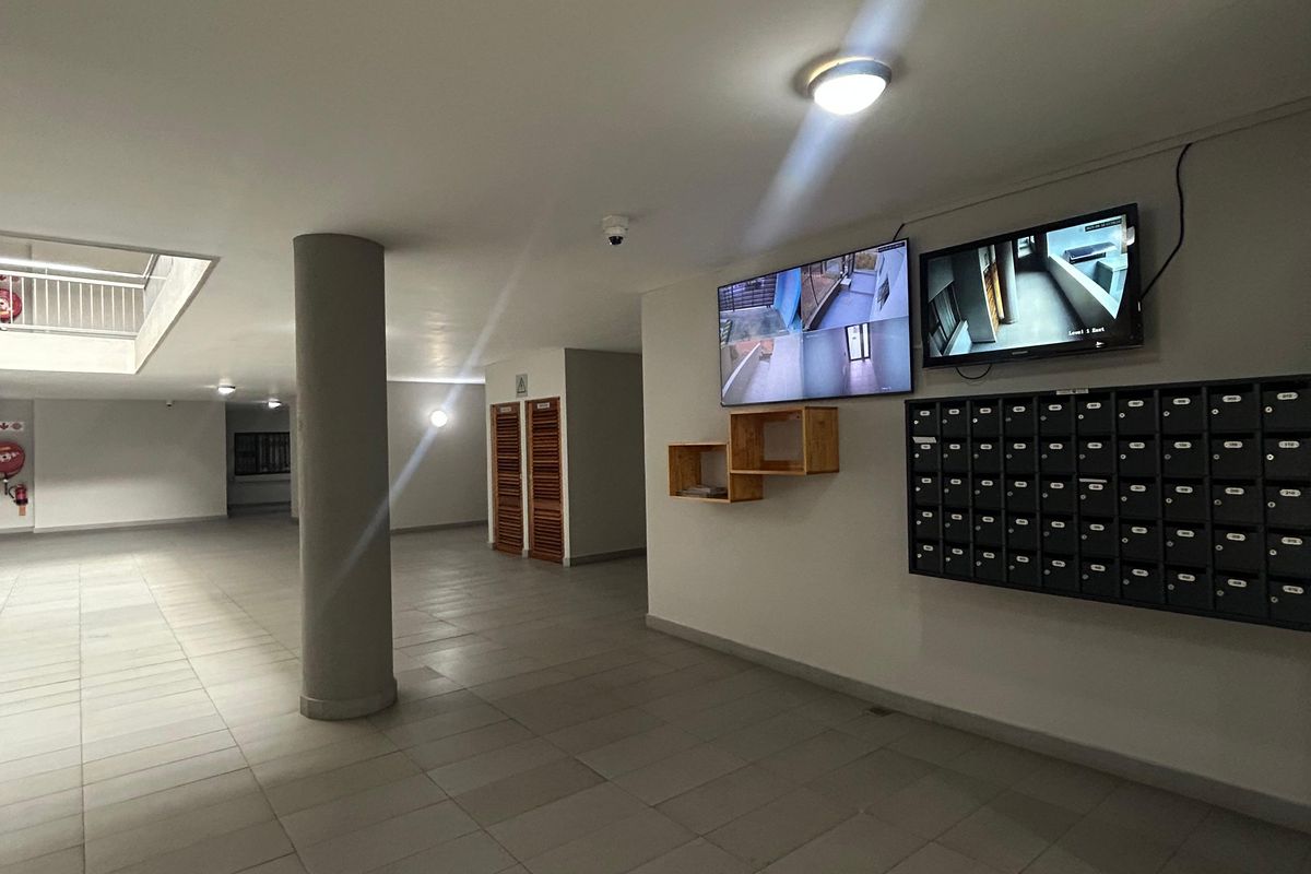 A clean and well-maintained apartment building entrance lobby featuring a wall-mounted mailbox bank and security monitoring screens.