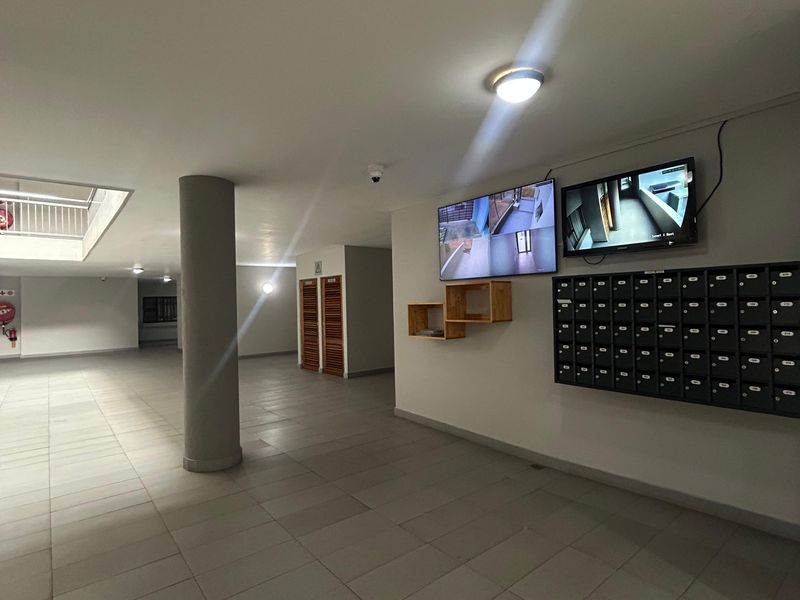 A clean and well-maintained apartment building entrance lobby featuring a wall-mounted mailbox bank and security monitoring screens.