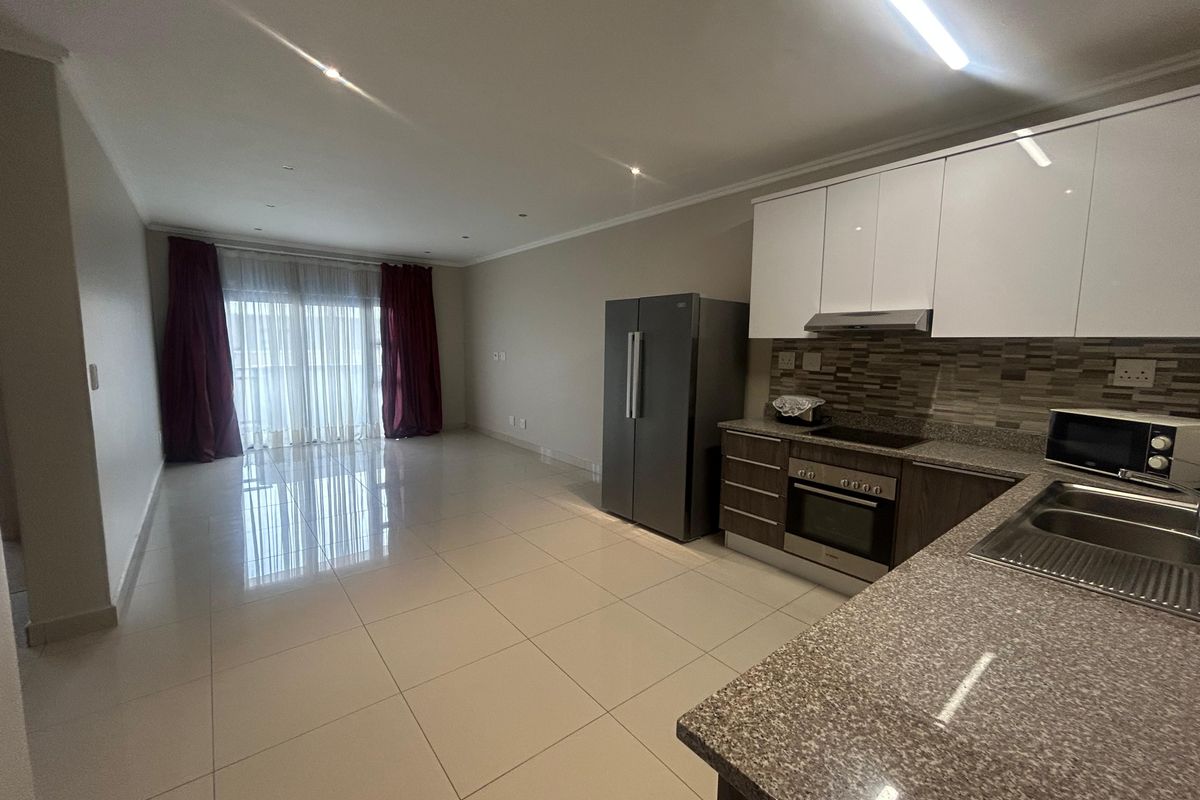 Spacious open-plan living area featuring a modern kitchen with granite countertops, built-in oven, hob, and extractor fan, leading to a bright balcony.