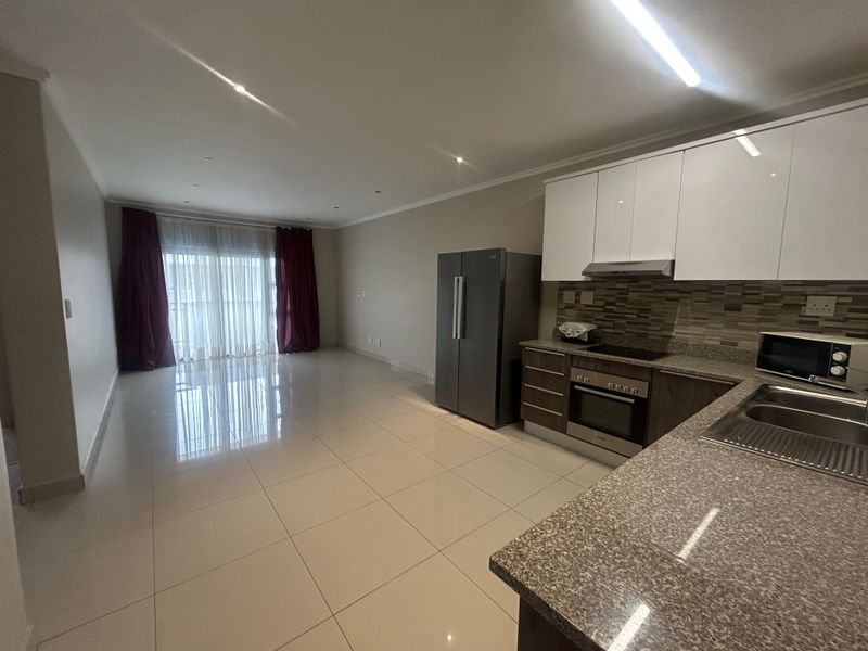Spacious open-plan living area featuring a modern kitchen with granite countertops, built-in oven, hob, and extractor fan, leading to a bright balcony.