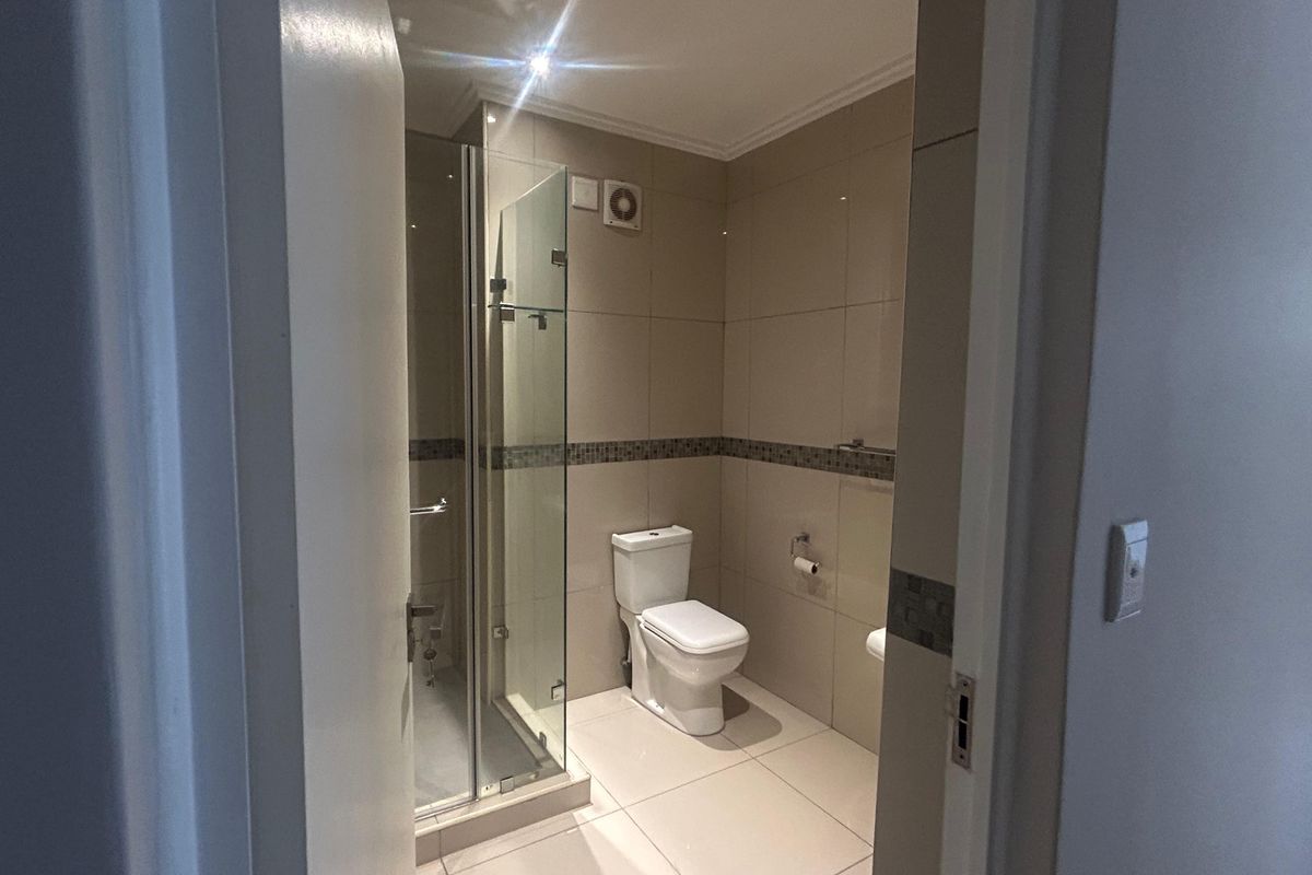 A clean, modern bathroom featuring a glass-enclosed shower, neutral wall and floor tiling, and integrated extractor fan.