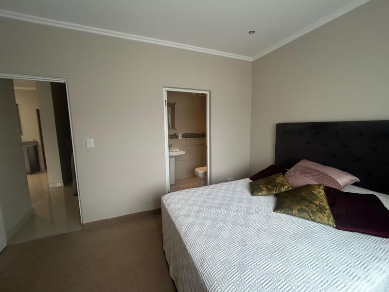 A well-maintained bedroom featuring neutral wall tones, coved ceilings, recessed lighting, and direct access to an en-suite bathroom.