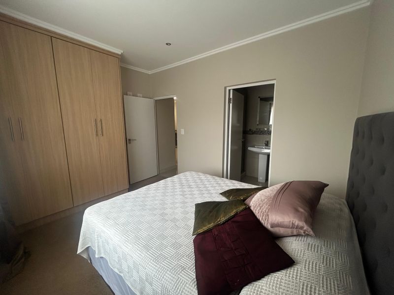 A well-maintained bedroom featuring built-in wooden wardrobes, neutral wall finishes, and direct access to an en-suite bathroom.