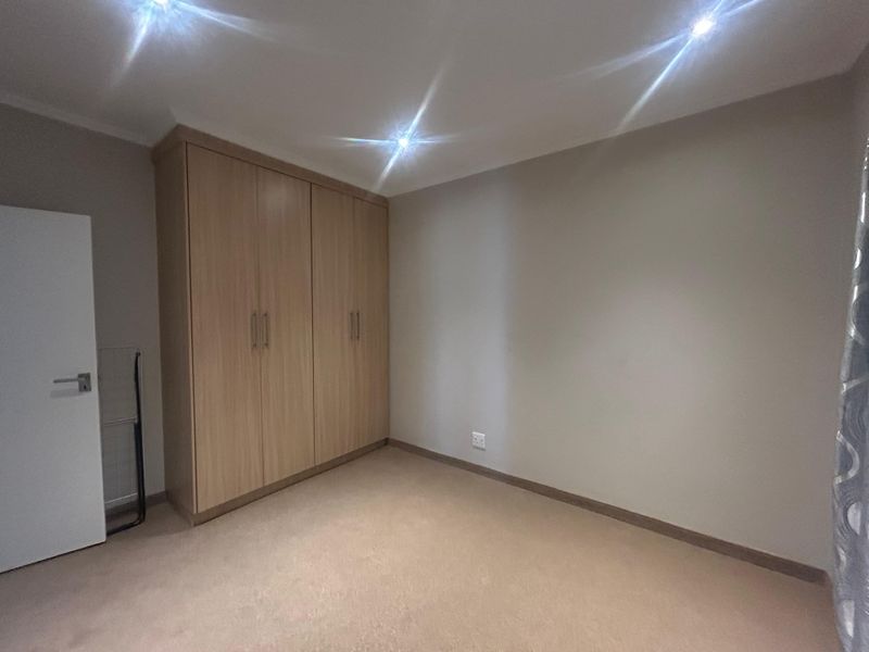 A clean, empty bedroom featuring neutral carpeting, built-in wooden cupboards, and modern recessed downlighting.