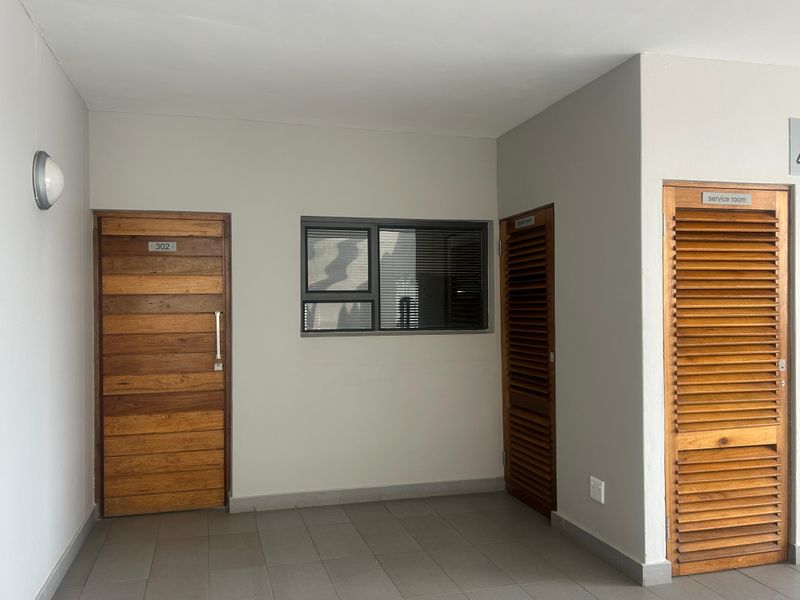 A clean apartment entrance lobby featuring tiled flooring, a timber front door, and louvered service doors.