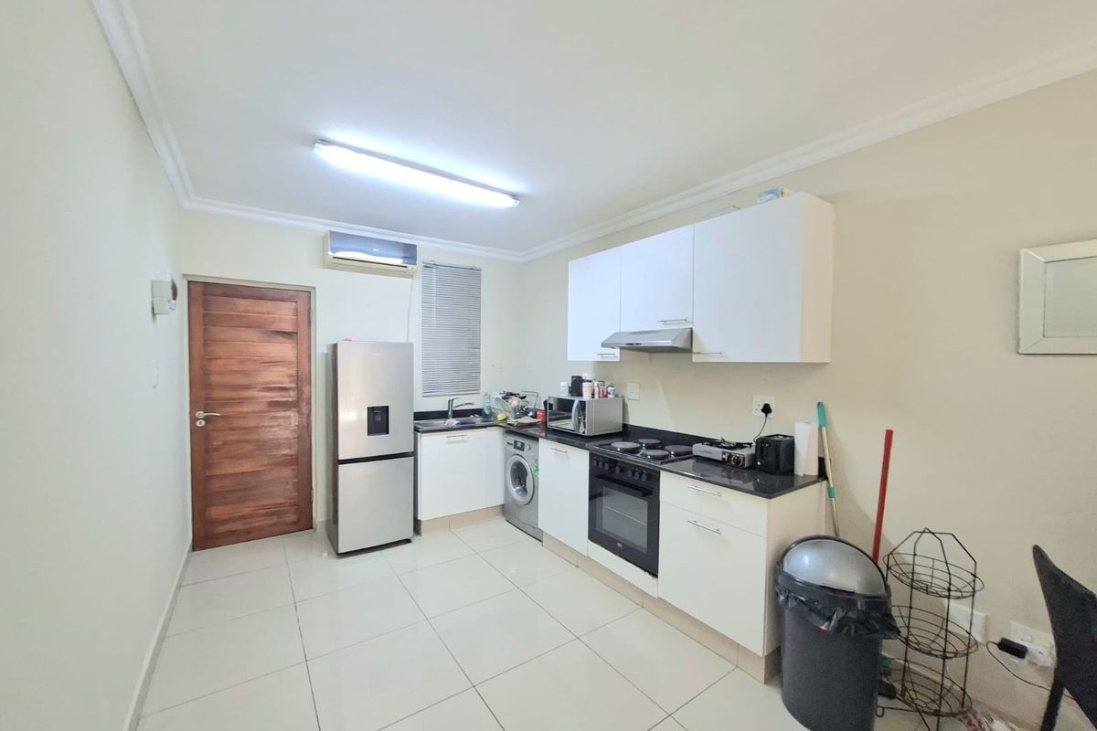 A functional kitchen featuring white cabinetry, dark countertops, integrated oven and hob, tiled flooring, and an air conditioning unit.