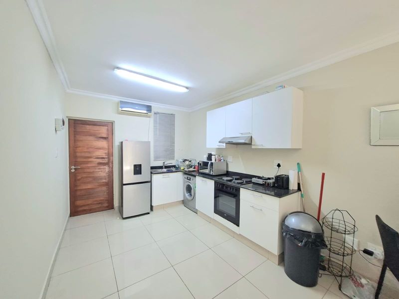 A functional kitchen featuring white cabinetry, dark countertops, integrated oven and hob, tiled flooring, and an air conditioning unit.