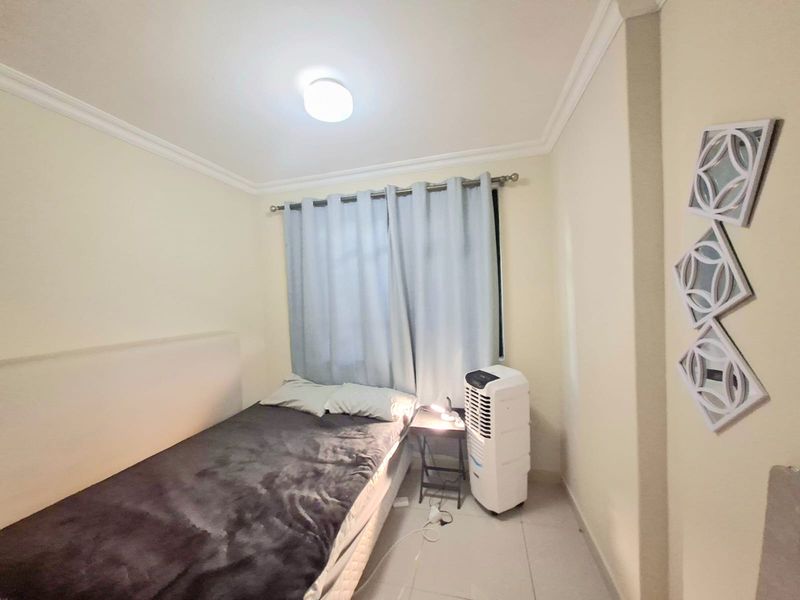 A compact bedroom featuring tiled flooring, crown molding, and a neutral color palette, providing a functional and well-lit sleeping space.