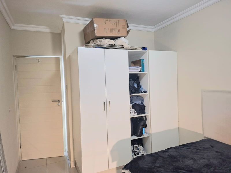 A bedroom featuring a white built-in wardrobe with open shelving, crown molding, and tiled flooring.