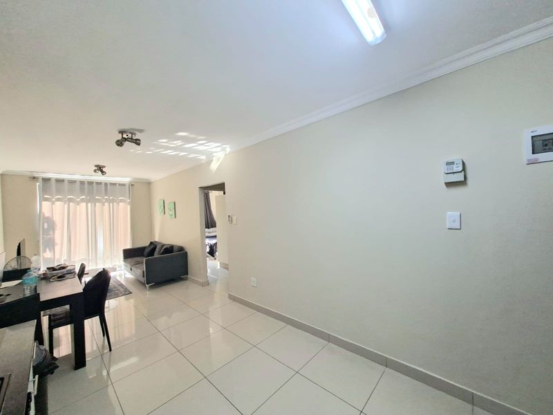 An open-plan living and dining area featuring tiled flooring, coved ceilings, and access to a balcony through sliding glass doors.
