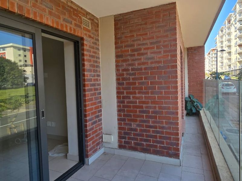 A modern balcony featuring a glass balustrade, exposed brick walls, and tiled flooring, providing an outdoor extension to the apartment living space.