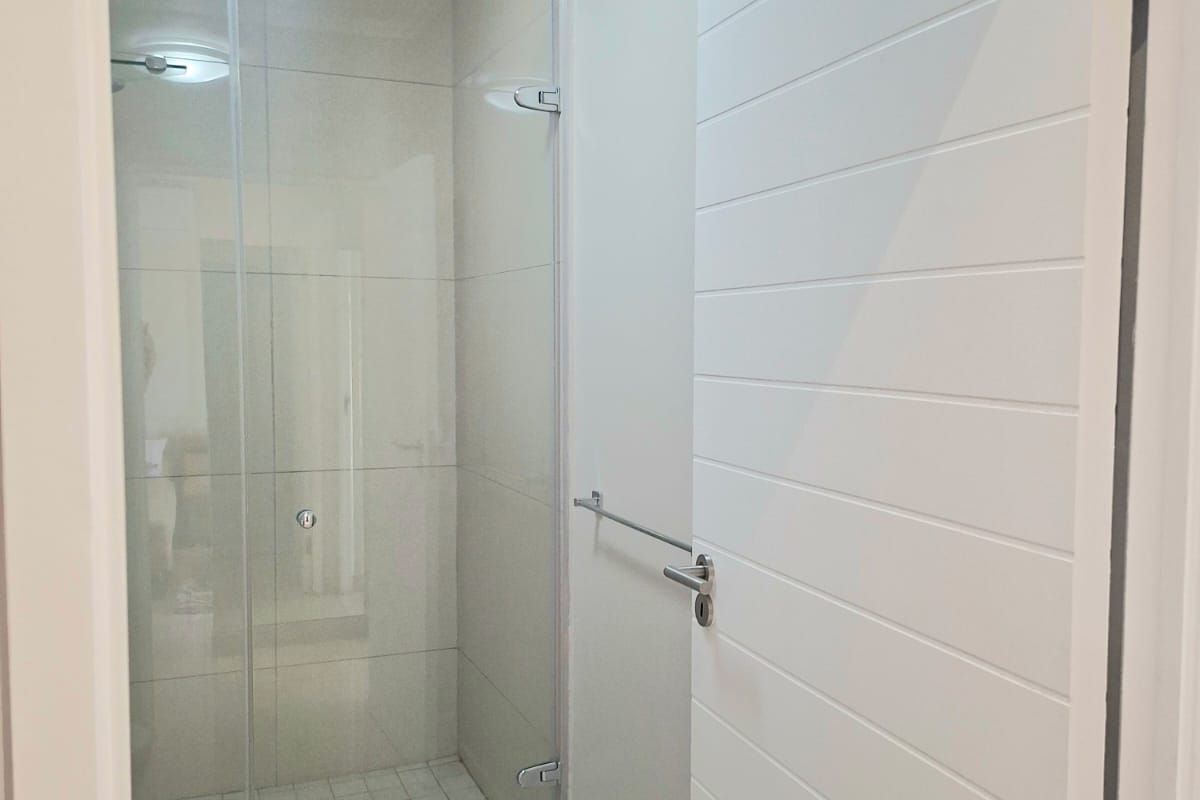 A clean and modern bathroom featuring a glass-enclosed shower with tiled flooring and a contemporary horizontal panel door.