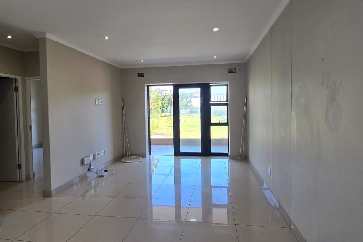 A spacious, empty living area featuring neutral tiled floors, recessed lighting, and a large sliding glass door providing access to the exterior.
