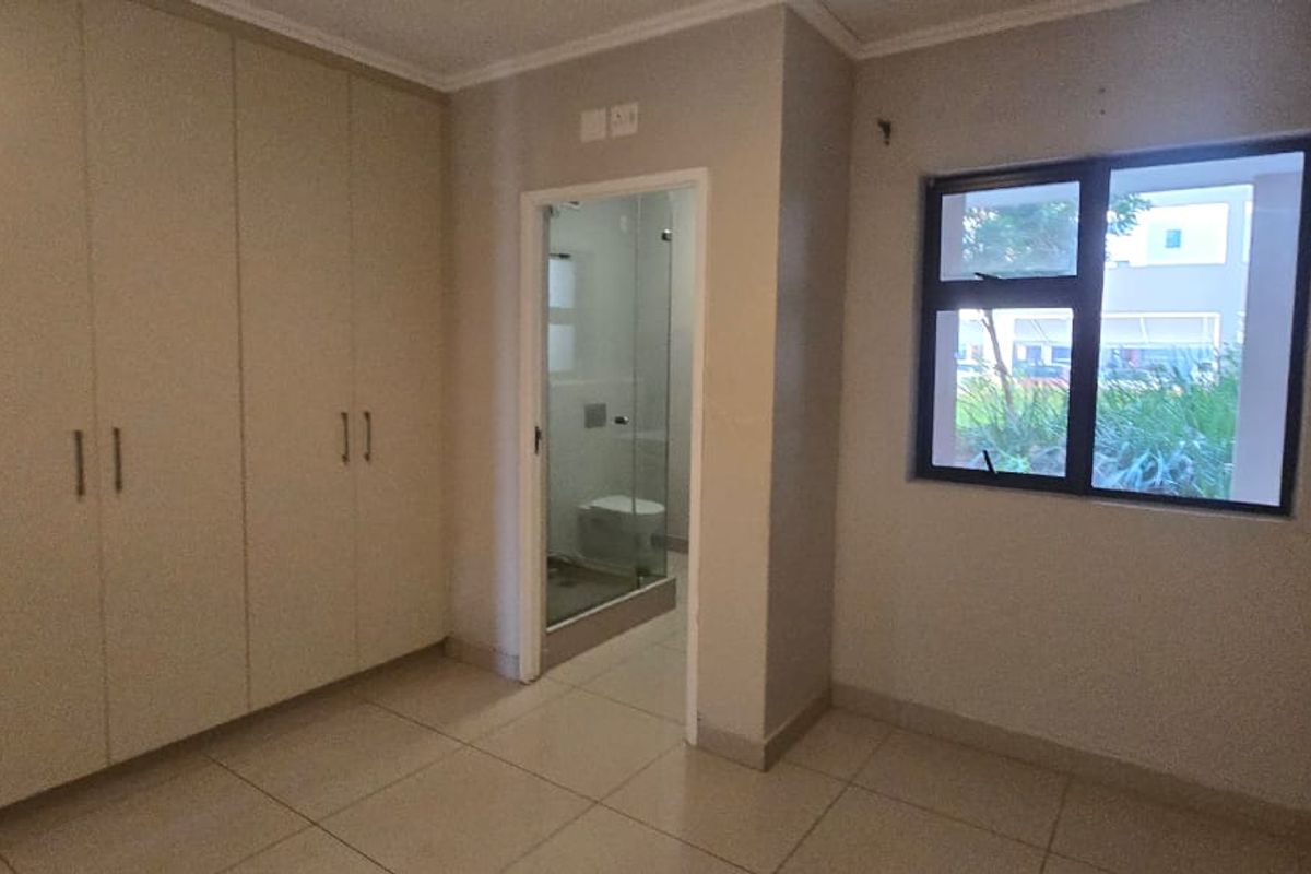 A clean, empty bedroom featuring built-in cupboards, tiled flooring, and an en-suite bathroom with a glass shower enclosure.