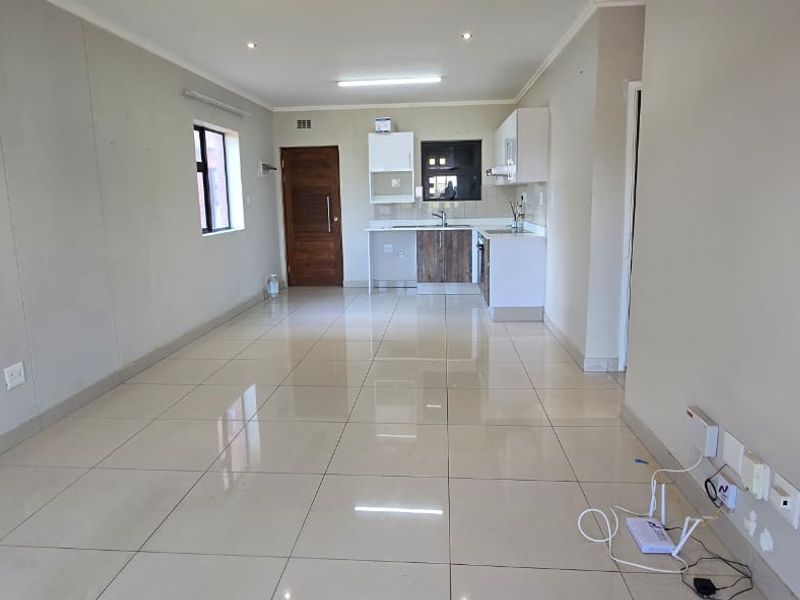 An open-plan living and kitchen area featuring tiled flooring, recessed lighting, and modern kitchen cabinetry with built-in appliances.