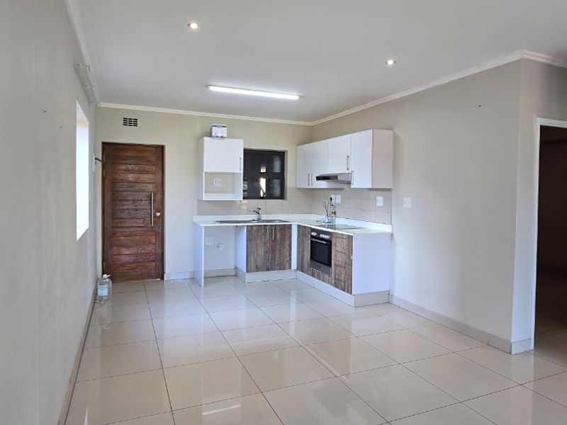 An open-plan kitchen and living area featuring neutral walls, tiled flooring, and modern built-in cabinetry with integrated appliances.