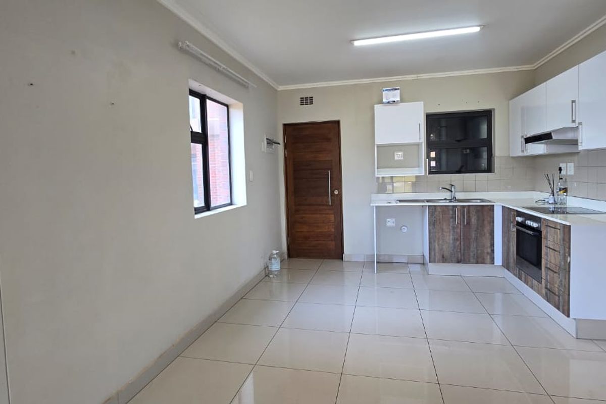 A clean, empty kitchen featuring modern two-tone cabinetry, built-in oven, extractor fan, and tiled flooring, offering a functional and neutral space.