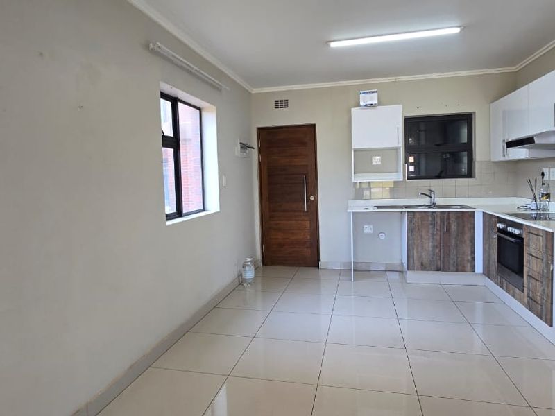 A clean, empty kitchen featuring modern two-tone cabinetry, built-in oven, extractor fan, and tiled flooring, offering a functional and neutral space.
