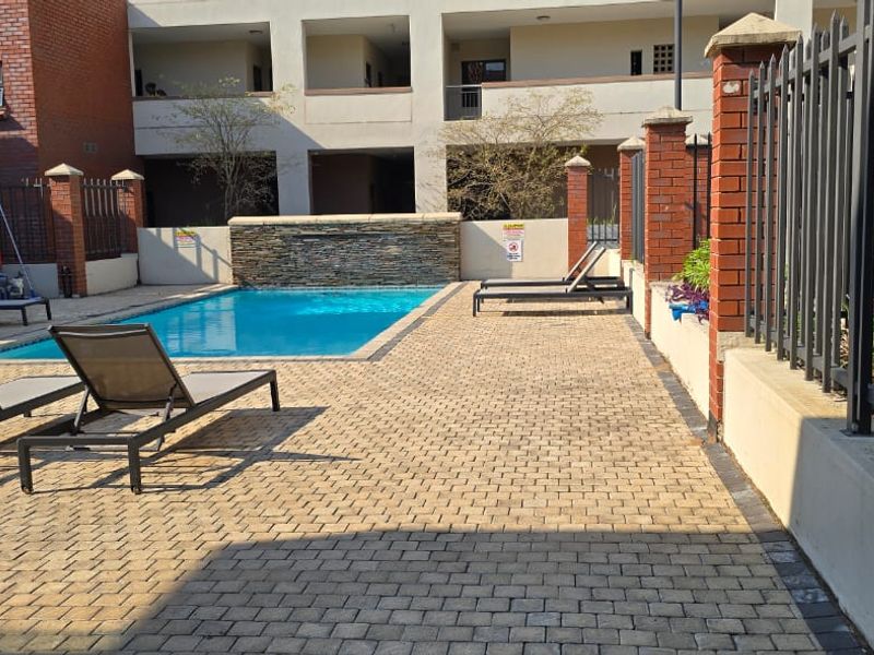 Communal swimming pool area featuring a stone water feature, paved deck, and secure brick and metal perimeter fencing.