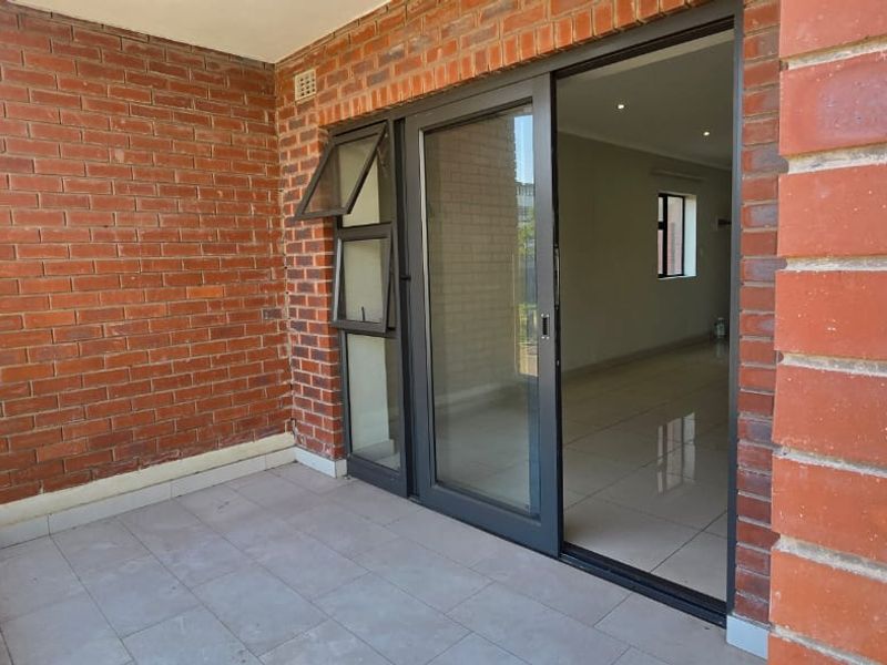A clean, modern balcony featuring exposed brick walls, tiled flooring, and a glass balustrade, providing seamless access to the interior living space.