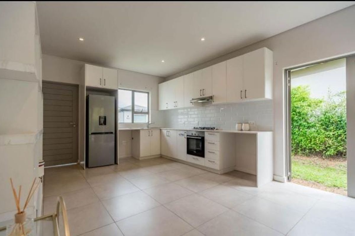 Modern kitchen featuring white cabinetry, subway tile backsplash, built-in oven and hob, tiled flooring, and direct access to the garden through a sliding door.