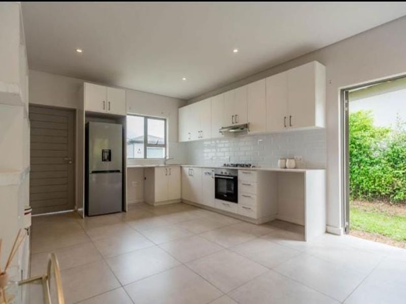 Modern kitchen featuring white cabinetry, subway tile backsplash, built-in oven and hob, tiled flooring, and direct access to the garden through a sliding door.