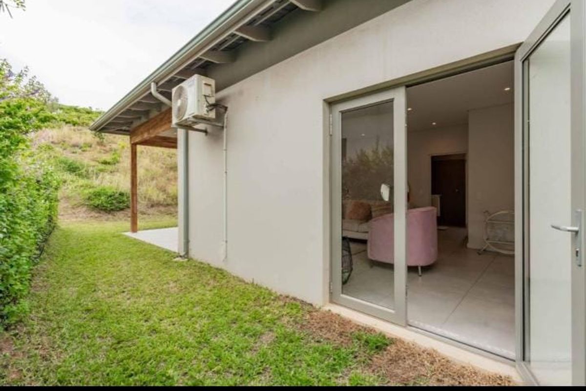 Rear exterior view of the townhouse featuring a small lawn, tiled patio area, and sliding glass doors providing access to the interior living space.