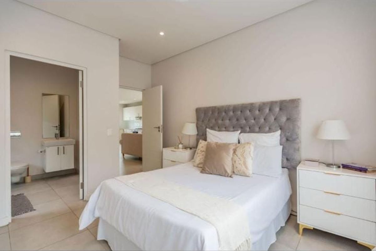 A well-maintained bedroom featuring neutral tones, tiled flooring, recessed lighting, and an adjoining en-suite bathroom with a modern vanity.