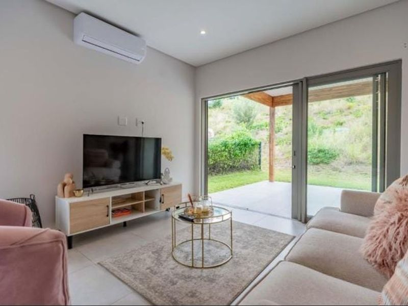 Modern living room featuring tiled floors, a wall-mounted air conditioner, and large sliding glass doors providing seamless access to the outdoor patio area.
