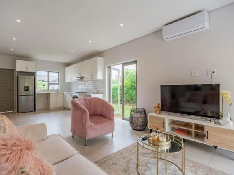 Modern open-plan living area featuring tiled floors, recessed lighting, a split-system air conditioner, and a functional kitchen with subway tile backsplash and direct garden access.