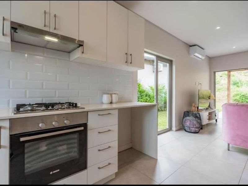 Modern open-plan kitchen featuring sleek white cabinetry, subway tile backsplash, gas hob, and integrated oven, flowing seamlessly into a bright living area with garden access.