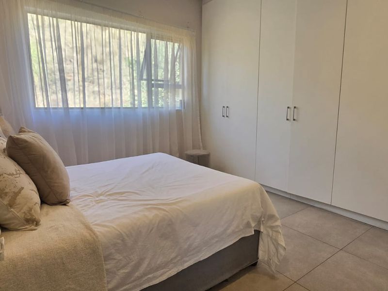A well-maintained bedroom featuring neutral tiled flooring, ample built-in cupboard storage, and a large window allowing for natural light.