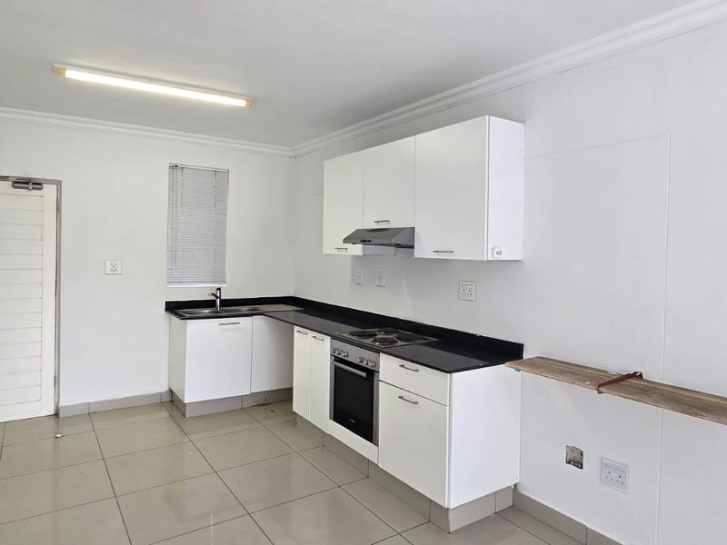 A clean, functional kitchen featuring white cabinetry, black countertops, built-in oven and hob, and tiled flooring in a bright, open-plan layout.